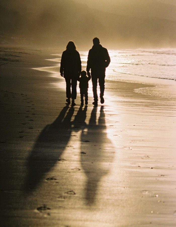 Família caminhando de mãos dadas na beira da praia ao entardecer