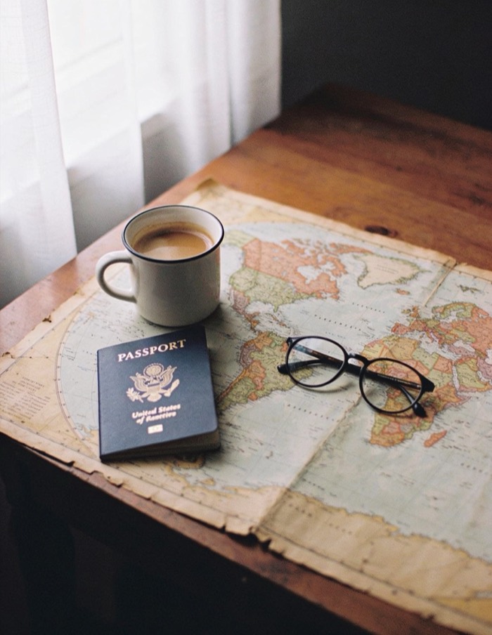 Mapa-múndi de papel sobre a mesa com passaporte, óculos e uma xícara de café