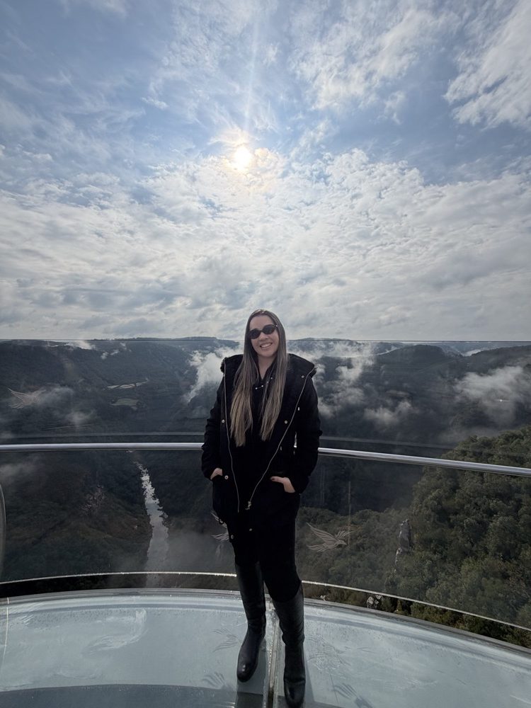 Vanessa, da Nosso Roteiro, sorrindo em um mirante de vidro sobre um cânion